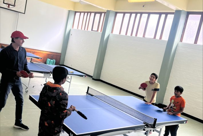 One adult playing table tennis with 3 children