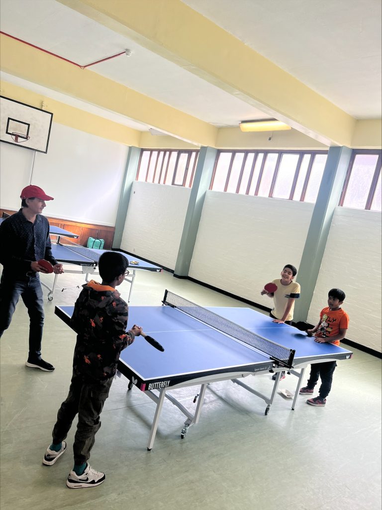 One adult playing table tennis with 3 children
