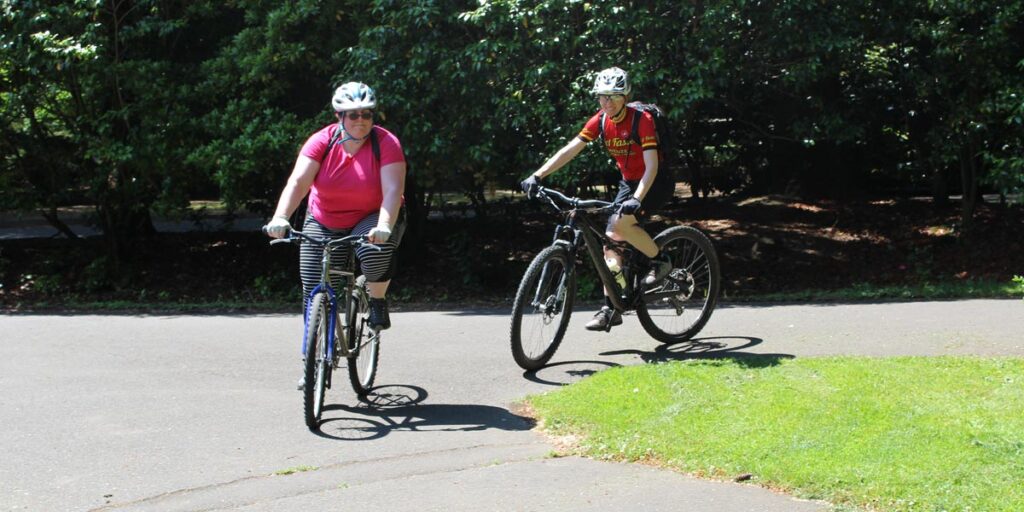 Two people cycling & smiling in sunshine